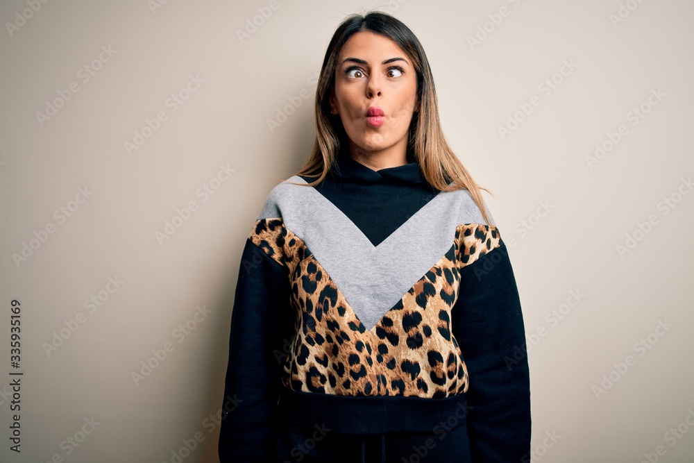 Fototapeta premium Young beautiful woman wearing casual sweatshirt standing over isolated white background making fish face with lips, crazy and comical gesture. Funny expression.