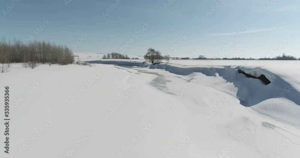 Winter river under snow cover melting a little among snow field and forest / at sunny frozen spring time - Aerial drone view Winter river under snow cover melting a little among snow field and forest / at sunny frozen spring time - Aerial drone view