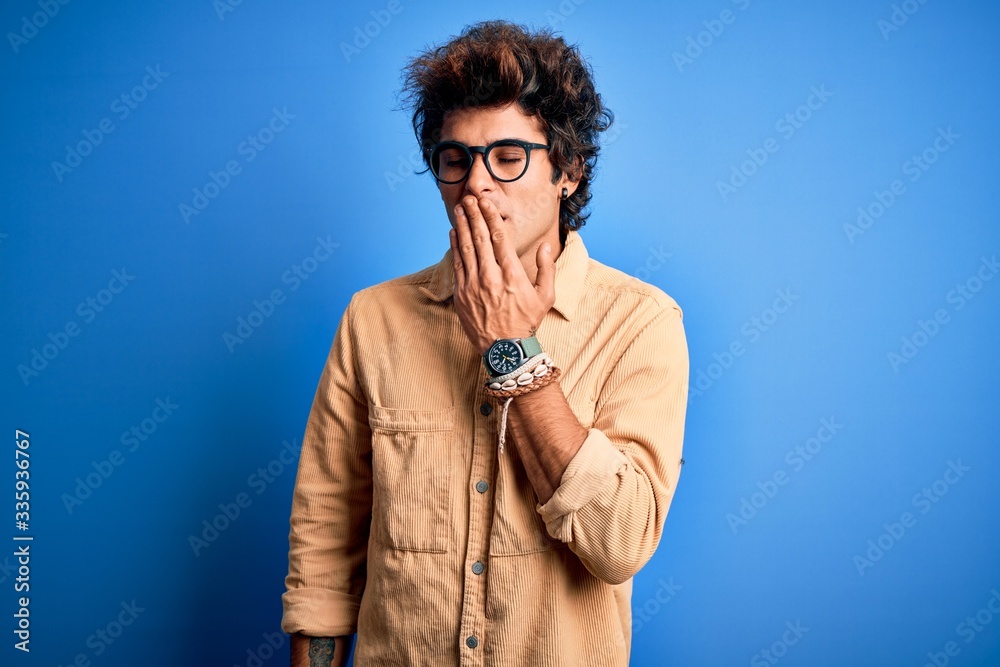 Young handsome man wearing casual shirt standing over isolated blue background bored yawning tired covering mouth with hand. Restless and sleepiness. Young handsome man wearing casual shirt standing over isolated blue background bored yawning tired covering mouth with hand. Restless and sleepiness.