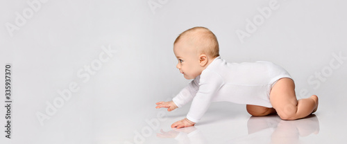 Chubby ginger baby boy in bodysuit, barefoot. He smiling, creeping on floor isolated on white background. Close up, copy space photo