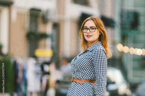 Street lights. Retro portrait young woman in checkered fashioned dress, bokeh of light bulbs on background. fun, smile, beautiful makeup. Poor vision and myopia. stylish woman at european street