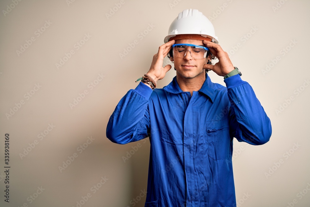Young constructor man wearing uniform and security helmet over isolated white background with hand on head for pain in head because stress. Suffering migraine.