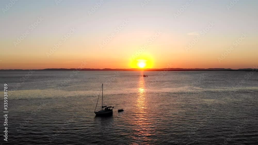 Cinematic Aerial sunset shot of sun behind hills, ocean and sailboat. Itaparica Island, Bahia, Brazil. Drone moving backward Cinematic Aerial sunset shot of sun behind hills, ocean and sailboat. Itaparica Island, Bahia, Brazil. Drone moving backward
