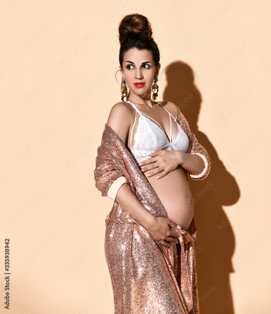 Pregnant woman with bright make-up, in earrings, white sexy lingerie and  golden robe. Posing against beige background. Close up Stock-Foto | Adobe  Stock