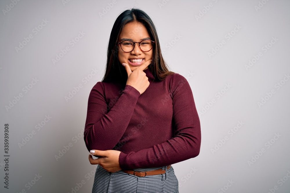 Beautiful asian business woman wearing casual sweater and glasses over white background looking confident at the camera smiling with crossed arms and hand raised on chin. Thinking positive. Beautiful asian business woman wearing casual sweater and glasses over white background looking confident at the camera smiling with crossed arms and hand raised on chin. Thinking positive.