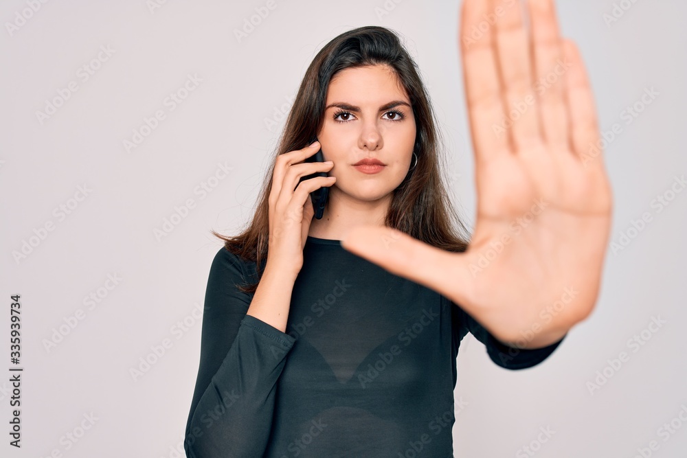 Young beautiful woman having a conversation talking on smartphone ove isolated background with open hand doing stop sign with serious and confident expression, defense gesture Young beautiful woman having a conversation talking on smartphone ove isolated background with open hand doing stop sign with serious and confident expression, defense gesture