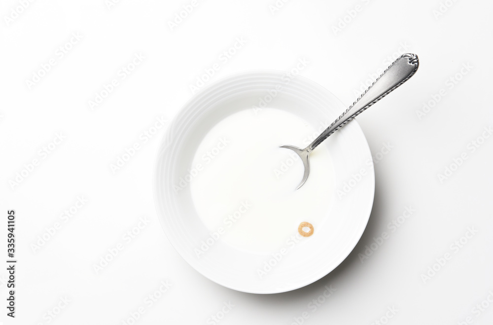 Flat lay white cereal bowl with spoon and one piece of cereal floating