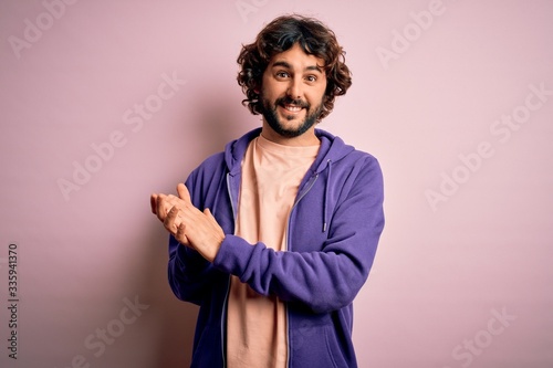 Young handsome sporty man with beard wearing casual sweatshirt over pink background clapping and applauding happy and joyful, smiling proud hands together