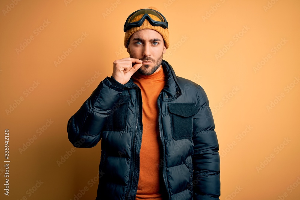 Young handsome skier man with beard wearing snow sportswear and ski goggles mouth and lips shut as zip with fingers. Secret and silent, taboo talking Young handsome skier man with beard wearing snow sportswear and ski goggles mouth and lips shut as zip with fingers. Secret and silent, taboo talking