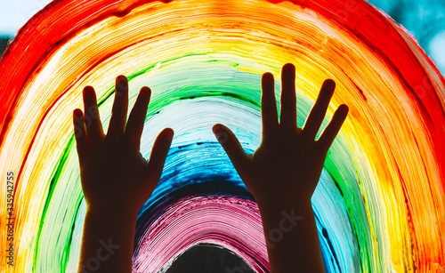 Photo Child hands touch painting rainbow on window.
