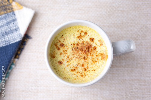 A top down view of a turmeric latte beverage in a white mug, in a restaurant or kitchen setting.