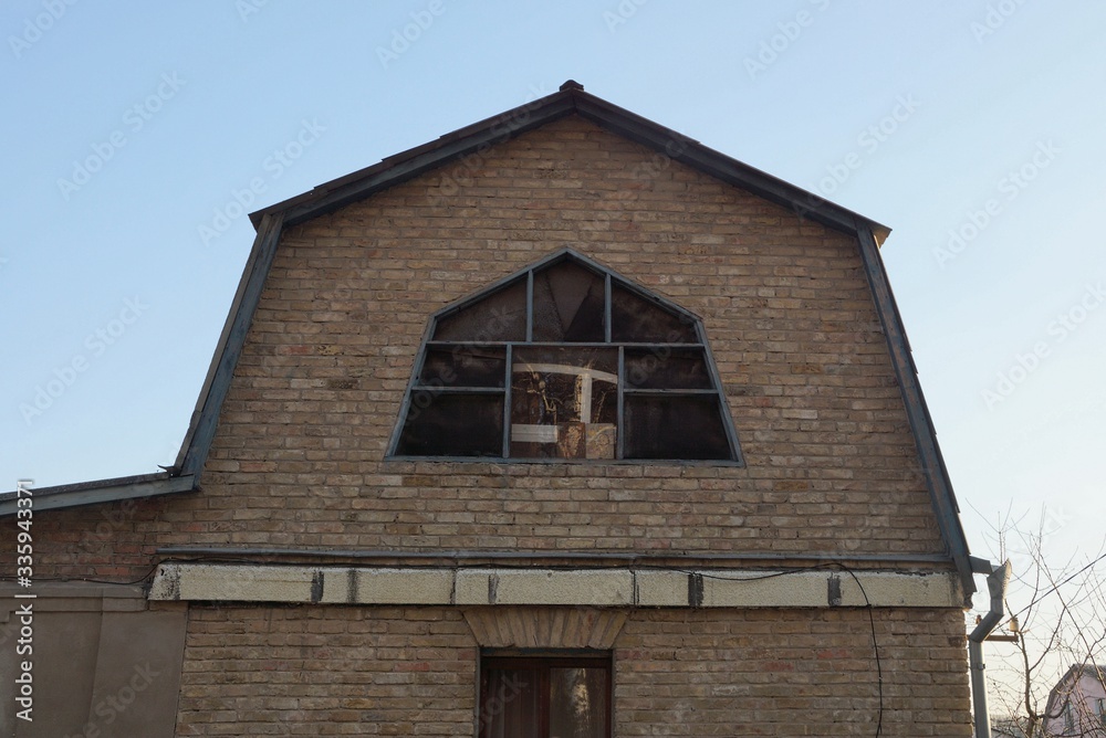 the attic of a rural private house of brown bricks with one large window against a blue sky