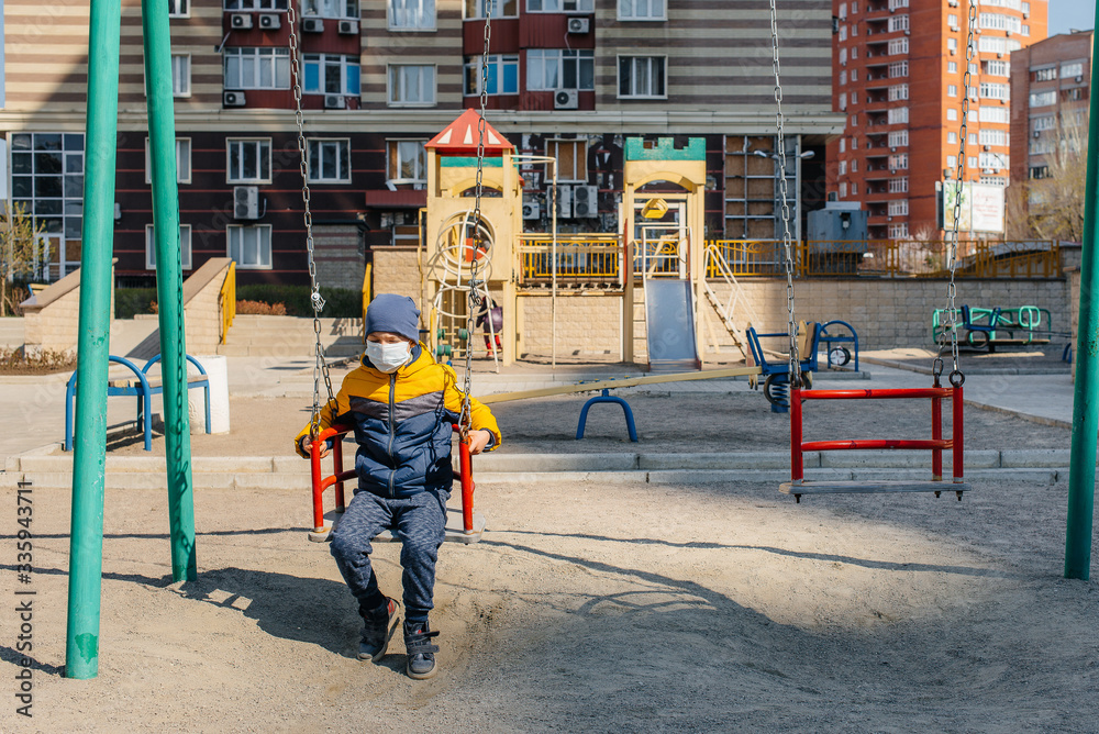 A small boy in a mask walks on the Playground during the quarantine. Stay at home