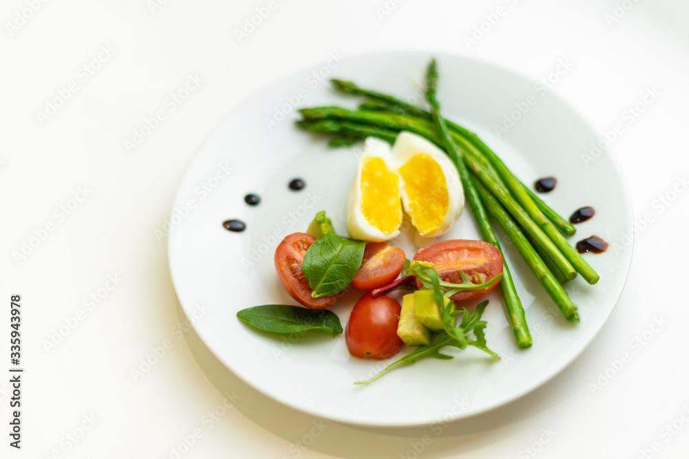 Boiled poached egg, cherry tomatoes, mix salad and asparagus on a white plate on an isolated white background. Healthy Diet Food Concept Boiled poached egg, cherry tomatoes, mix salad and asparagus on a white plate on an isolated white background. Healthy Diet Food Concept
