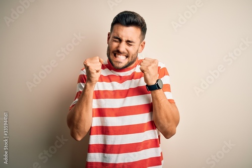 Young handsome man wearing casual striped t-shirt standing over isolated white background excited for success with arms raised and eyes closed celebrating victory smiling. Winner concept.