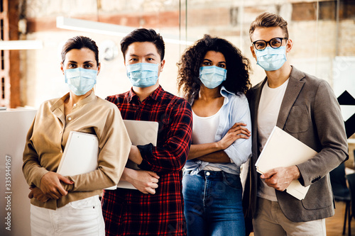 Multiracial young people in medical masks standing in office