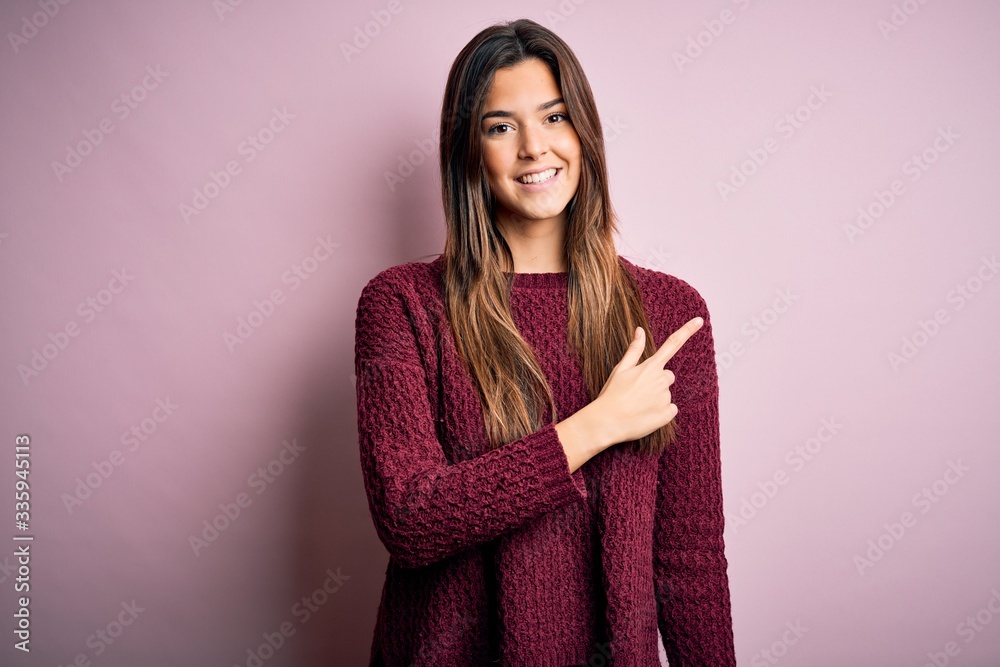 Young beautiful girl wearing casual sweater over isolated pink background cheerful with a smile on face pointing with hand and finger up to the side with happy and natural expression Young beautiful girl wearing casual sweater over isolated pink background cheerful with a smile on face pointing with hand and finger up to the side with happy and natural expression