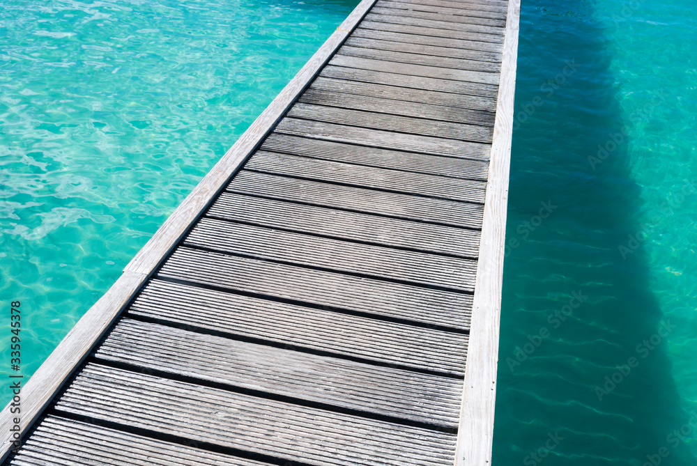 Abstract diagonal view of shallow tropical blue crystal waters sparkling under a weathered wooden bridge