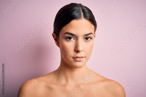 Young beautiful girl standing over isolated pink background with a confident expression on smart face thinking serious