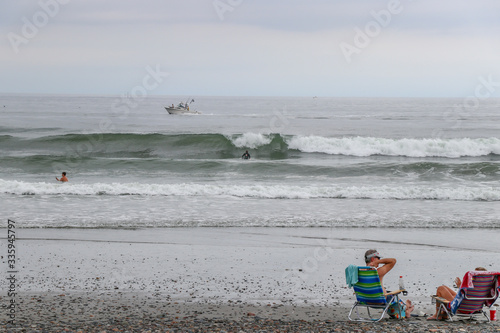 couple sit in lawn chair watching surfers in ocean on cloudy day