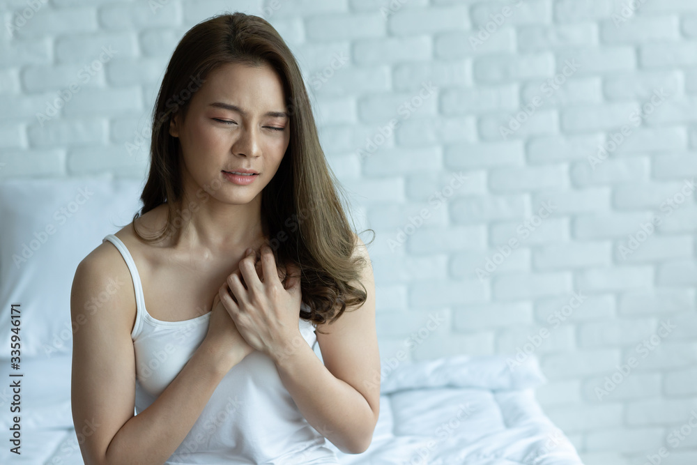 Asian Woman Has Chest Pain Sitting on bed in bedroom after wake up in morning.Health care concept. Asian Woman Has Chest Pain Sitting on bed in bedroom after wake up in morning.Health care concept.