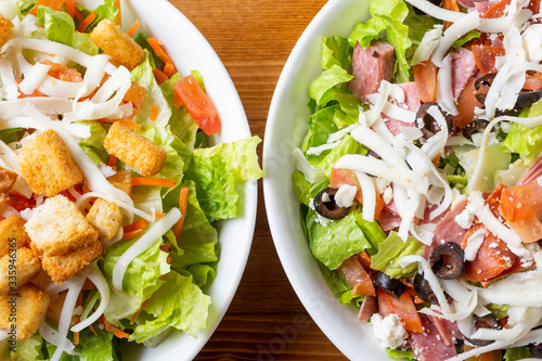 A top down view of a garden salad on the left and an antipasto salad on the right side of the frame, in a restaurant or kitchen setting.