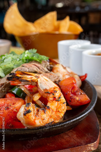 A closeup view of a prawn on a surf and turf style fajita skillet plate, in a restaurant or kitchen setting.