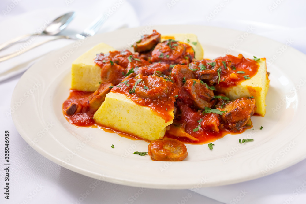 A view of a plate of polenta and sausage, in a restaurant or kitchen setting. A view of a plate of polenta and sausage, in a restaurant or kitchen setting.