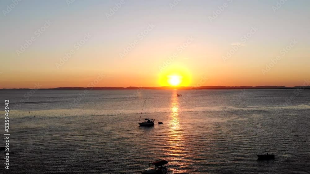 Majestic Aerial sunset shot of sun behind hills, ocean and sailboat. Itaparica Island, Bahia, Brazil. Drone moving forwards Majestic Aerial sunset shot of sun behind hills, ocean and sailboat. Itaparica Island, Bahia, Brazil. Drone moving forwards