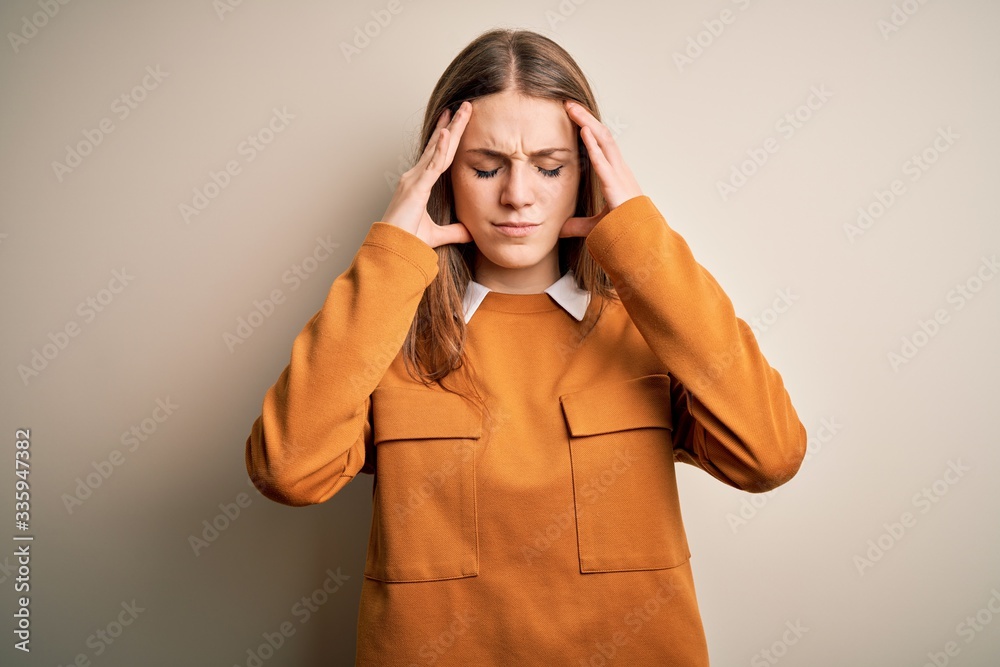Young beautiful redhead woman wearing casual sweater over isolated white background with hand on head for pain in head because stress. Suffering migraine.