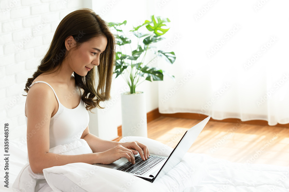 Beautiful asian woman working on a laptop sitting on the bed in the house.Woman checking social apps and working.Work from home concept. Beautiful asian woman working on a laptop sitting on the bed in the house.Woman checking social apps and working.Work from home concept.