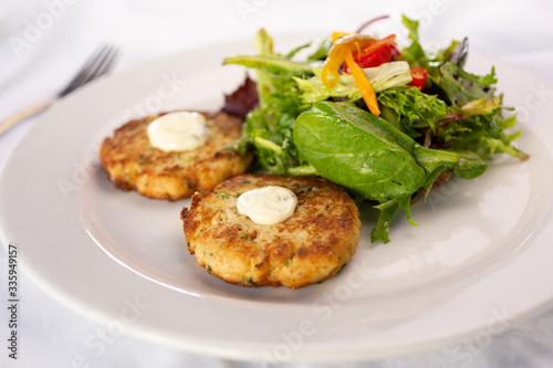 A closeup view of a plate of crab cakes next to a garden salad.