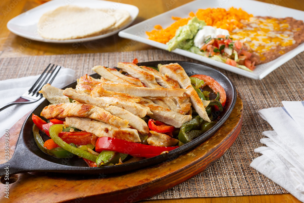 A view of a chicken fajita skillet plate, with a side of rice and beans, in a restaurant or kitchen setting.