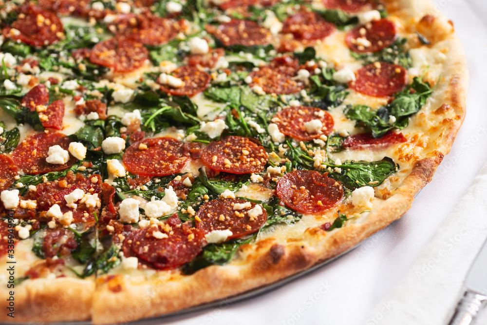A closeup view of a Greek style pizza pie, featuring pepperoni, spinach and feta cheese, in a restaurant or kitchen setting. A closeup view of a Greek style pizza pie, featuring pepperoni, spinach and feta cheese, in a restaurant or kitchen setting.