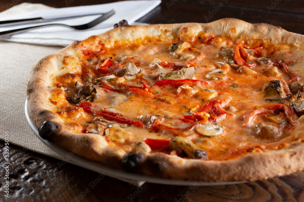 A view of a rustic pizza with mushrooms, peppers, and artichokes, in a restaurant or kitchen setting.