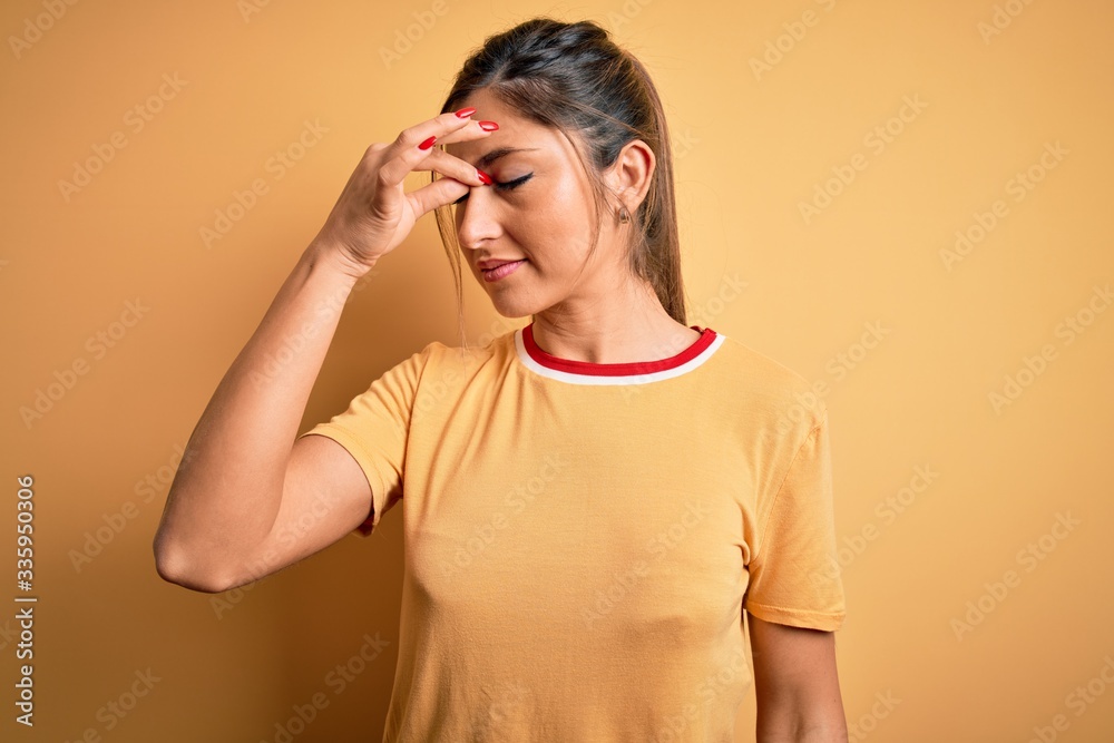 Young beautiful athletic woman wearing casual t-shirt and ponytail over yellow background tired rubbing nose and eyes feeling fatigue and headache. Stress and frustration concept. Young beautiful athletic woman wearing casual t-shirt and ponytail over yellow background tired rubbing nose and eyes feeling fatigue and headache. Stress and frustration concept.