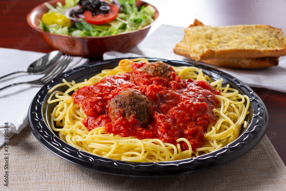 A view of a spaghetti and meatballs dinner, with a side salad and garlic bread, in a restaurant or kitchen setting.