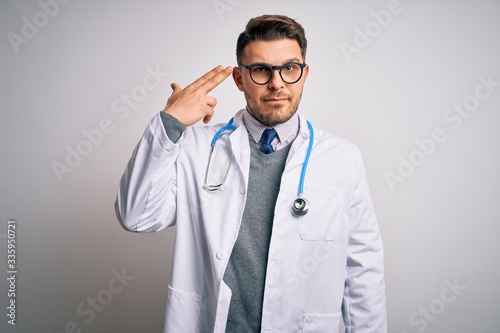 Young doctor man with blue eyes wearing medical coat and stethoscope over isolated background Shooting and killing oneself pointing hand and fingers to head like gun, suicide gesture.