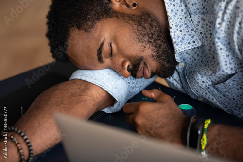 Close up of tired african American male worker or student feel fatigue exhaustion fall asleep at workplace, exhausted biracial man overwhelmed with work take nap sleep at office desk, overwork concept photo