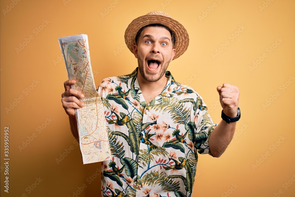 Young man on vacation wearing summer hat holding and looking at tourist map over yellow background screaming proud and celebrating victory and success very excited, cheering emotion Young man on vacation wearing summer hat holding and looking at tourist map over yellow background screaming proud and celebrating victory and success very excited, cheering emotion