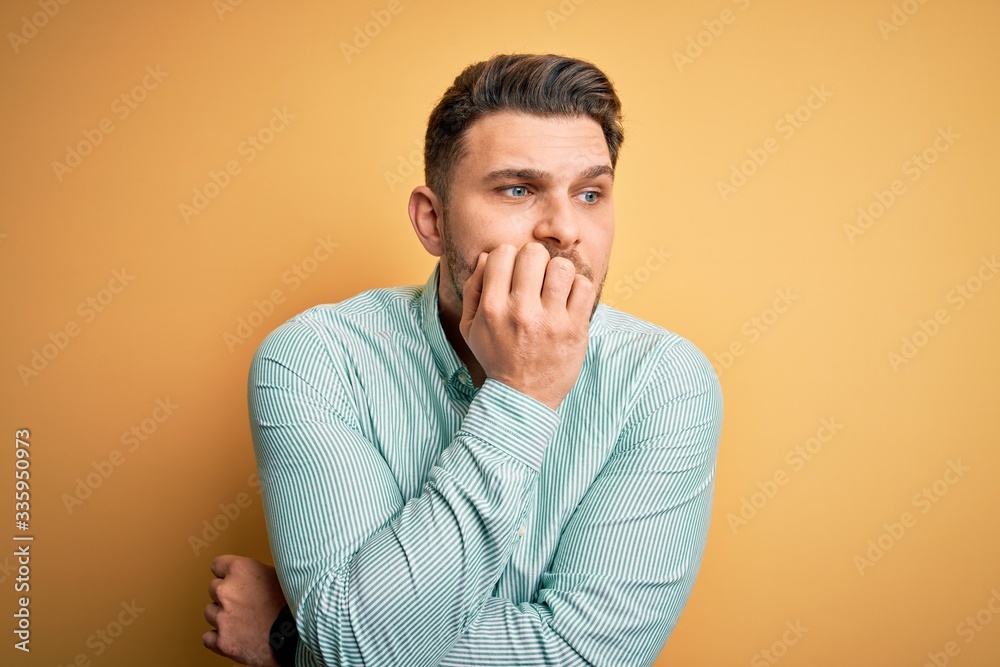 Young business man with blue eyes wearing elegant green shirt over yellow background looking stressed and nervous with hands on mouth biting nails. Anxiety problem. Young business man with blue eyes wearing elegant green shirt over yellow background looking stressed and nervous with hands on mouth biting nails. Anxiety problem.
