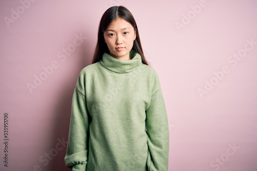 Young beautiful asian woman wearing green winter sweater over pink solated background Relaxed with serious expression on face. Simple and natural looking at the camera. © Krakenimages.com