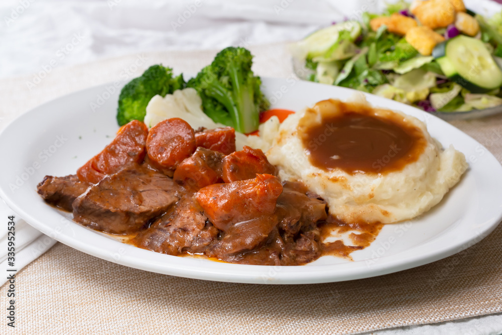 A view of a plate of pot roast dinner, with a side salad, in a restaurant or kitchen setting. A view of a plate of pot roast dinner, with a side salad, in a restaurant or kitchen setting.