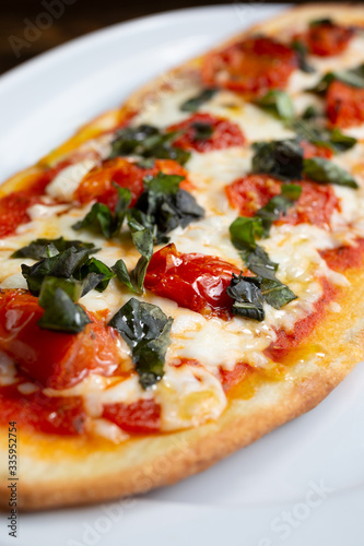 A view of a plate of margherita style flatbread pizza, in a restaurant or kitchen setting.