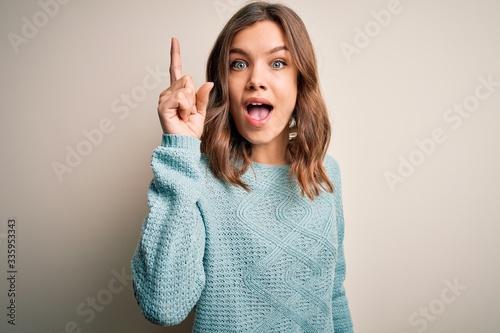 Young blonde girl wearing casual blue winter sweater over isolated background pointing finger up with successful idea. Exited and happy. Number one.