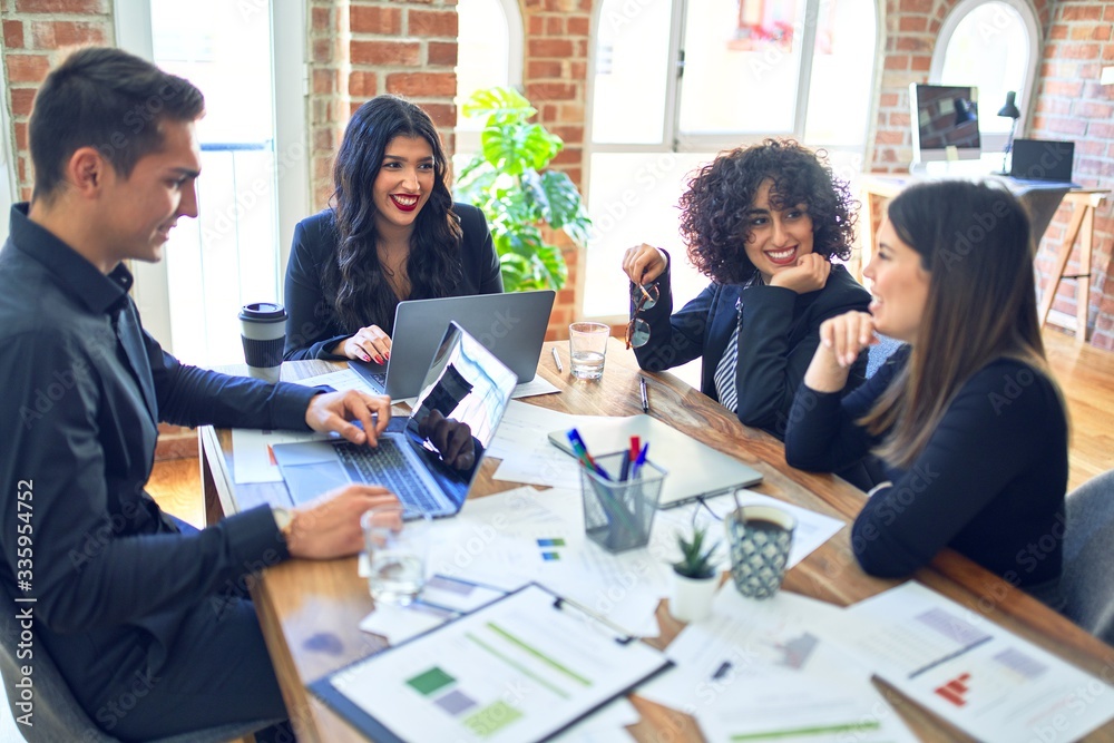 Group of business workers smiling happy and confident. Working together with smile on face using laptop and speaking at the office Group of business workers smiling happy and confident. Working together with smile on face using laptop and speaking at the office
