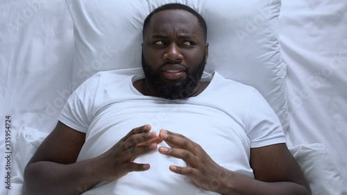 Pensive man drumming his fingers lying in bed, thinking over ideas, top-view