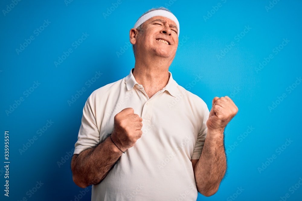 Middle age hoary sportsman doing sport wearing sportswear over isolated blue background excited for success with arms raised and eyes closed celebrating victory smiling. Winner concept.