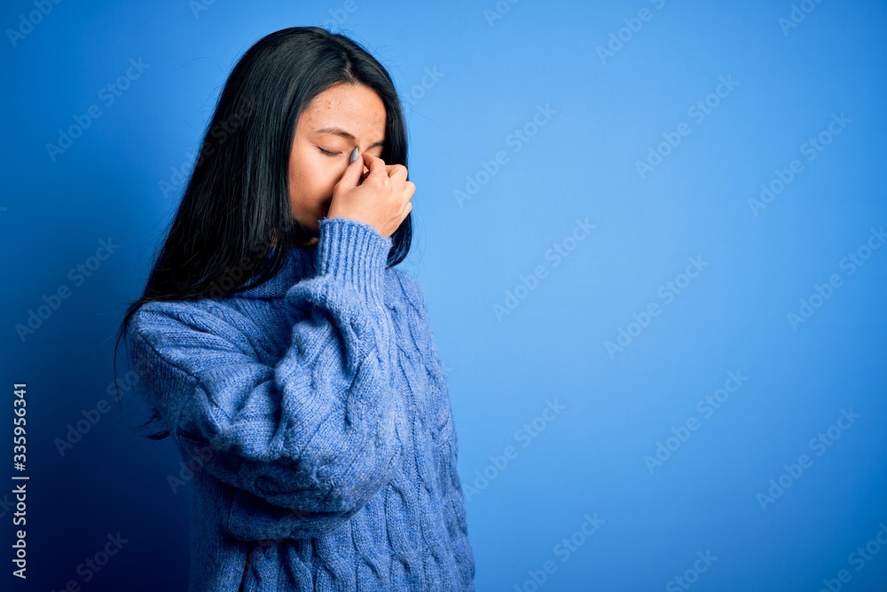 Young beautiful chinese woman wearing casual sweater over isolated blue background tired rubbing nose and eyes feeling fatigue and headache. Stress and frustration concept. Young beautiful chinese woman wearing casual sweater over isolated blue background tired rubbing nose and eyes feeling fatigue and headache. Stress and frustration concept.