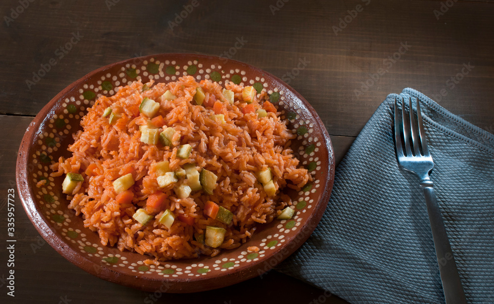 Mexican food, Mexican rice with vegetables and tomato puree on a mug plate or clay plate, with a blue napkin and a fork on the side Mexican food, Mexican rice with vegetables and tomato puree on a mug plate or clay plate, with a blue napkin and a fork on the side